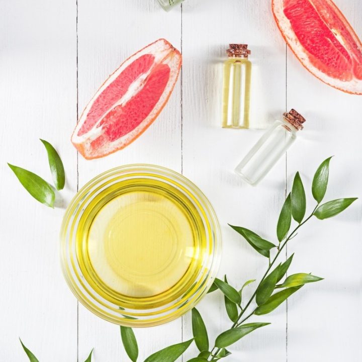 Essential oil in glass bottle with fresh, juicy grapefruit and green leaves-beauty treatment.