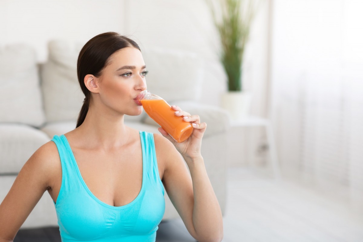 Fitness Girl Drinking Fruit Juice From Bottle Standing At Home; How To Blast Cellulite: The Truth That Nobody Is Telling You